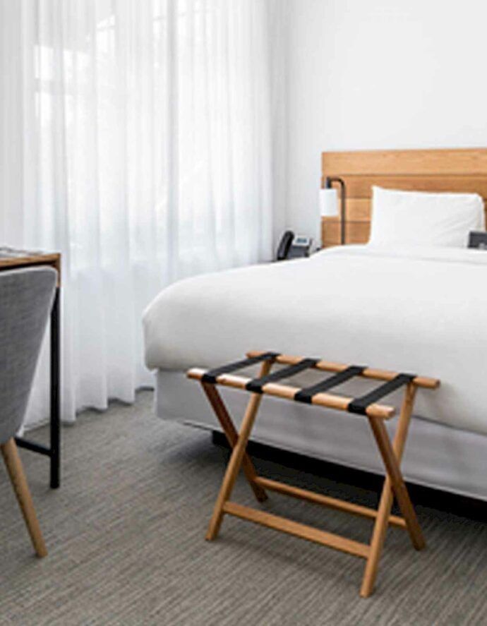 Hotel room with a bed, luggage rack, desk, and sheer curtains.