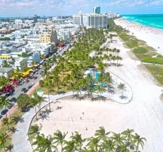 Aerial view of Miami Beach with turquoise water, white sand, palm trees, and buildings.